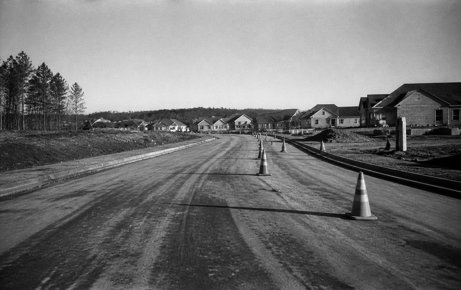 A newly built suburban road with construction cones and new housing in the distance